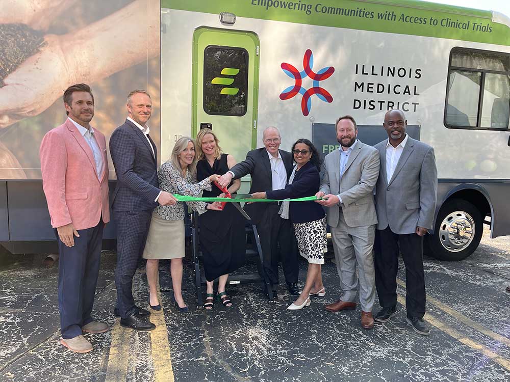 Bus with green EmVenio logo and Illinois Medical District logo and eight people cutting green ribbon