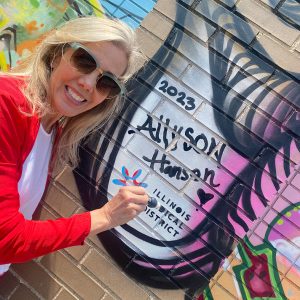 Allyson Hansen with marker and name written on brick exterior wall with graffiti
