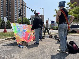 Chicago sidewalk with people standing around large plywood piece covered in colorful graffiti art