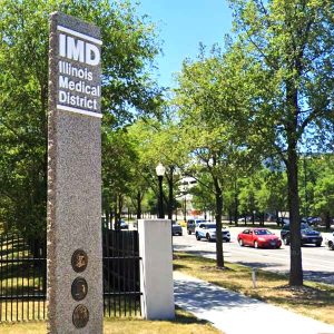 Outdoors, city street, large gray stone pillar that reads "IMD"